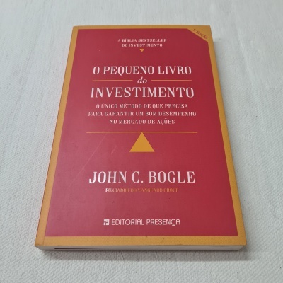 Livro vermelho 'O Pequeno Livro do Investimento' de John C. Bogle em superfície branca