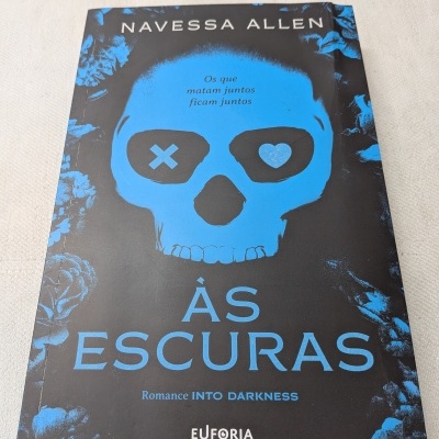 Livro ÀS ESCURAS com capa preta e azul e desenho de caveira.