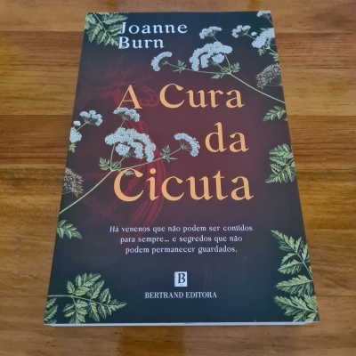 Livro 'A Cura da Cicuta' de Joanne Burn sobre superfície de madeira