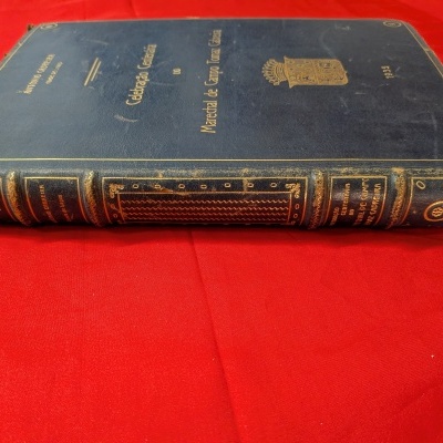 Livro capa dura azul escura com texto dourado e tecido vermelho ao fundo