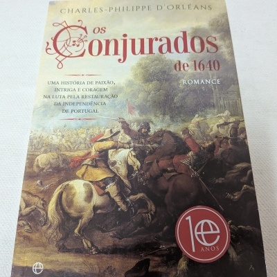 Capa de livro com ilustração de batalha, título Os Conjurados de 1640, selo 10 anos e texto descritivo