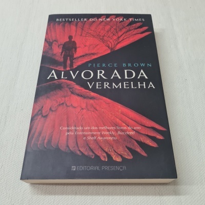 Livro 'Alvorada Vermelha' de capa preta com asas vermelhas em superfície branca