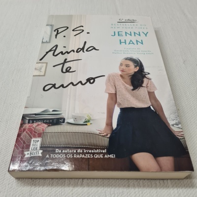 Capa do livro 'P.S. Ainda te amo' de Jenny Han com imagem de jovem sentada e livros ao fundo