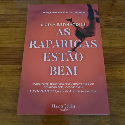 Capa vermelha de livro com título e texto em branco sobre mesa de madeira