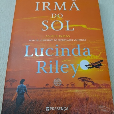 Capa do livro A Irmã do Sol de Lucinda Riley em tons laranja com campo e pessoa de costas