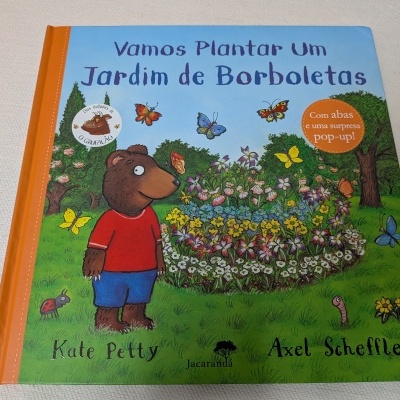 Capa de livro infantil com urso e borboletas num jardim colorido