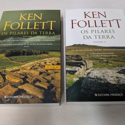 Dois livros em português, Ken Follett, Os Pilares da Terra, volumes I e II, com capas de paisagens rochosas e verdes.