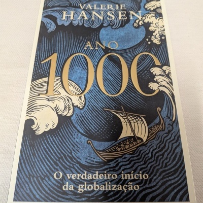 Capa de livro azul com barco, ondas e texto em dourado e bege