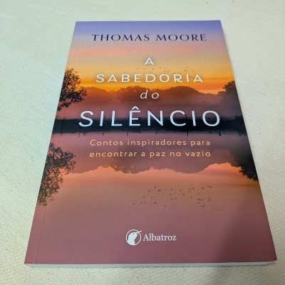 Livro 'A Sabedoria do Silêncio' de Thomas Moore com capa colorida e paisagem de pôr do sol