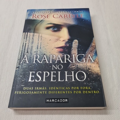 Capa do livro 'A Rapariga no Espelho' de Rose Carlyle com imagem de rosto de mulher detrás de vidro molhado.