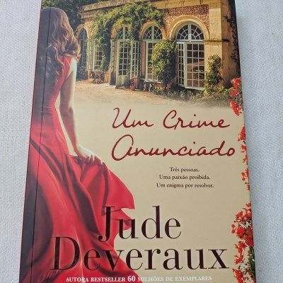 Capa do livro Um Crime Anunciado de Jude Deveraux com imagem de mulher de vestido vermelho e edifício antigo ao fundo
