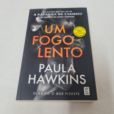 Capa de livro 'Um Fogo Lento' de Paula Hawkins com design preto, laranja e branco