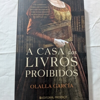 Capa do livro A Casa dos Livros Proibidos com ilustração de mulher com vestido antigo segurando livro antigo