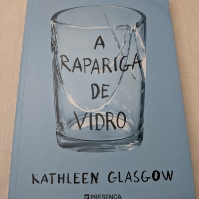 Capa de livro azul com copo de vidro partido e título A Rapariga de Vidro.