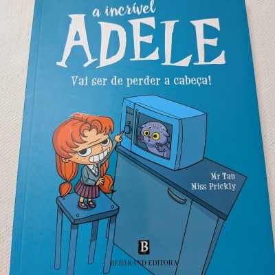 Capa de livro infantil azul com ilustração de menina ruiva e micro-ondas com gato dentro