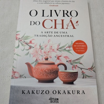 Capa de livro sobre chá com bule e chávena vermelhos decorativos e flores rosadas.