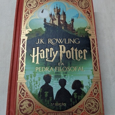 Capa do livro Harry Potter e a Pedra Filosofal com design vermelho, dourado e ilustração de castelo.