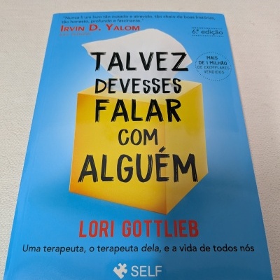 Capa de livro azul com título em letras pretas e vermelhas, ilustração de caixa amarela e papel branco, texto adicional em português.