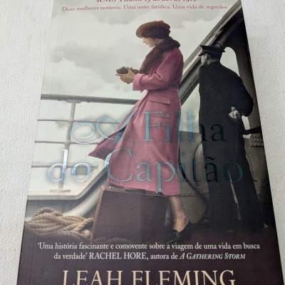 Capa de livro A Filha do Capitão com imagem de mulher de casaco rosa e homem de uniforme no convés de navio.