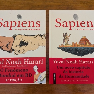Dois livros Sapiens de Yuval Noah Harari com capas brancas e vermelhas sobre mesa de madeira