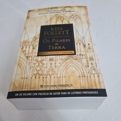 Livro 'Os Pilares da Terra' de Ken Follett com capa bege e desenhos arquitetónicos
