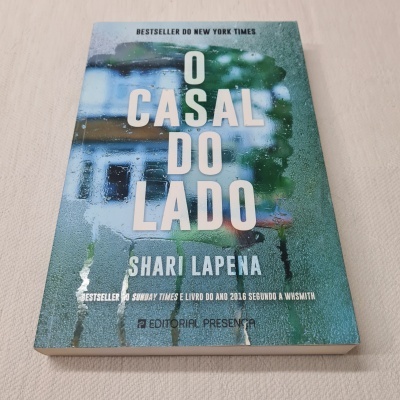 Livro 'O CASAL DO LADO' de Shari Lapena com capa azul esverdeada molhada