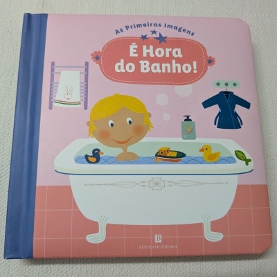 Capa de livro infantil rosa e azul com ilustração de criança na banheira e texto É Hora do Banho.