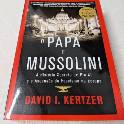 Livro O Papa e Mussolini com capa vermelha e foto em preto e branco da Basílica de São Pedro.