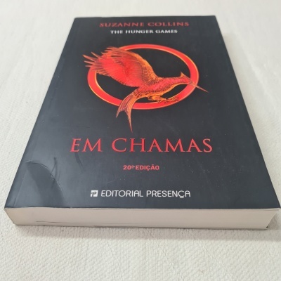 Livro 'EM CHAMAS' de capa preta com pássaro vermelho na frente