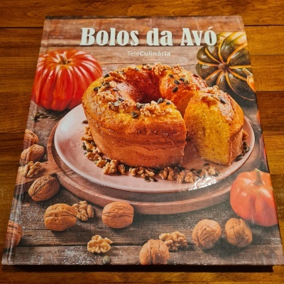 Capa de livro 'Bolos da Avó' com bolo e nozes sobre mesa de madeira