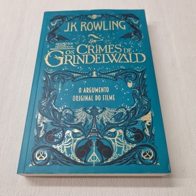 Livro 'Os Crimes de Grindelwald' de J.K. Rowling com capa azul-turquesa e texto dourado