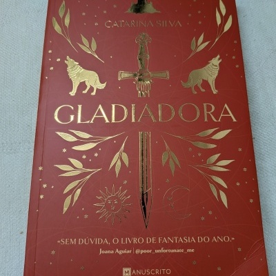 Capa de livro vermelha com texto e ilustrações douradas de espada, lobos, sol, lua e ramos