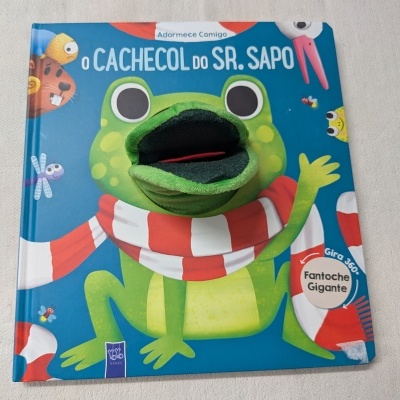 Capa de livro infantil com marioneta gigante de sapo e texto em português.
