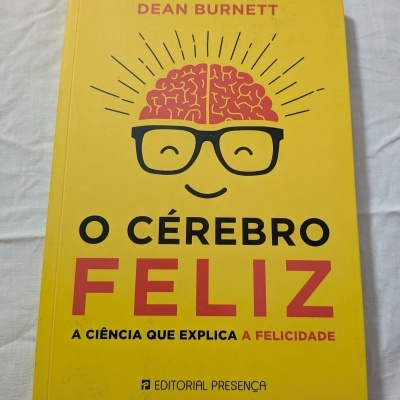 Capa de livro amarelo com título O CÉREBRO FELIZ e ilustração de cérebro com óculos e sorriso