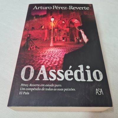 Capa do livro 'O Assédio' de Arturo Pérez-Reverte com imagem de rua em tons vermelhos e pretos
