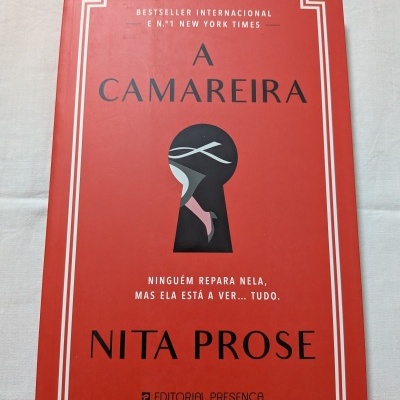 Capa do livro A CAMAREIRA de NITA PROSE, vermelha com ilustração em forma de fechadura e texto em preto e branco
