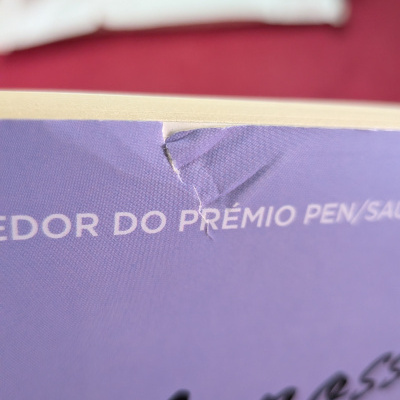 Livro com capa lilás danificada e texto parcialmente visível em branco e preto