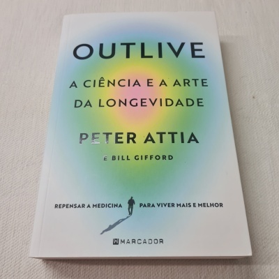 Livro OUTLIVE com capa branca e detalhes coloridos sobre superfície bege