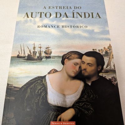 Capa do livro A Estreia do Auto da Índia com pintura de casal histórico e barco ao fundo