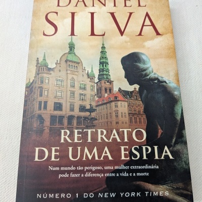 Capa de livro Retrato de uma Espia de Daniel Silva com edifícios e estátua