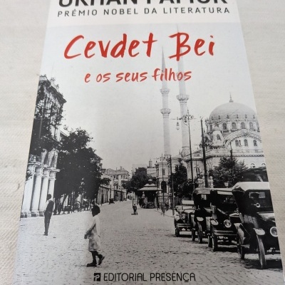 Livro Cevdet Bei e os seus filhos de Orhan Pamuk com fundo de foto antiga de rua.