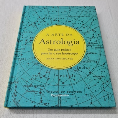 Capa de livro azul com constelações e círculo amarelo com texto do título 'A ARTE DA Astrologia'.