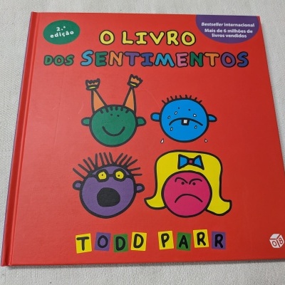 Capa de livro infantil vermelha com rostos coloridos e título O LIVRO DOS SENTIMENTOS.