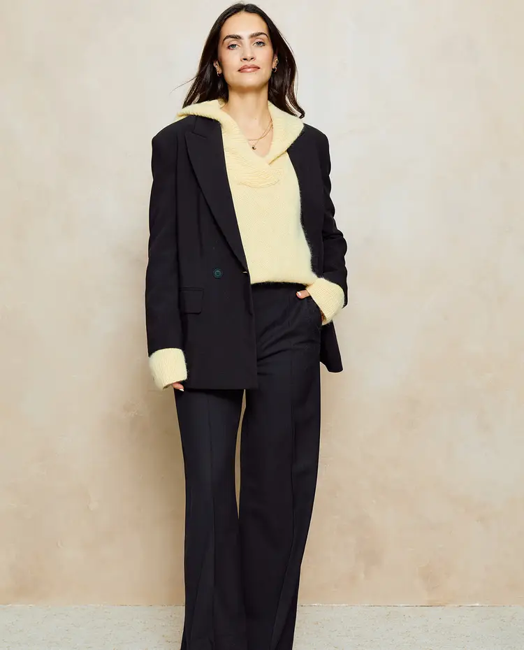 Mulher com blazer e calças pretas e camisola amarelo claro de malha felpuda