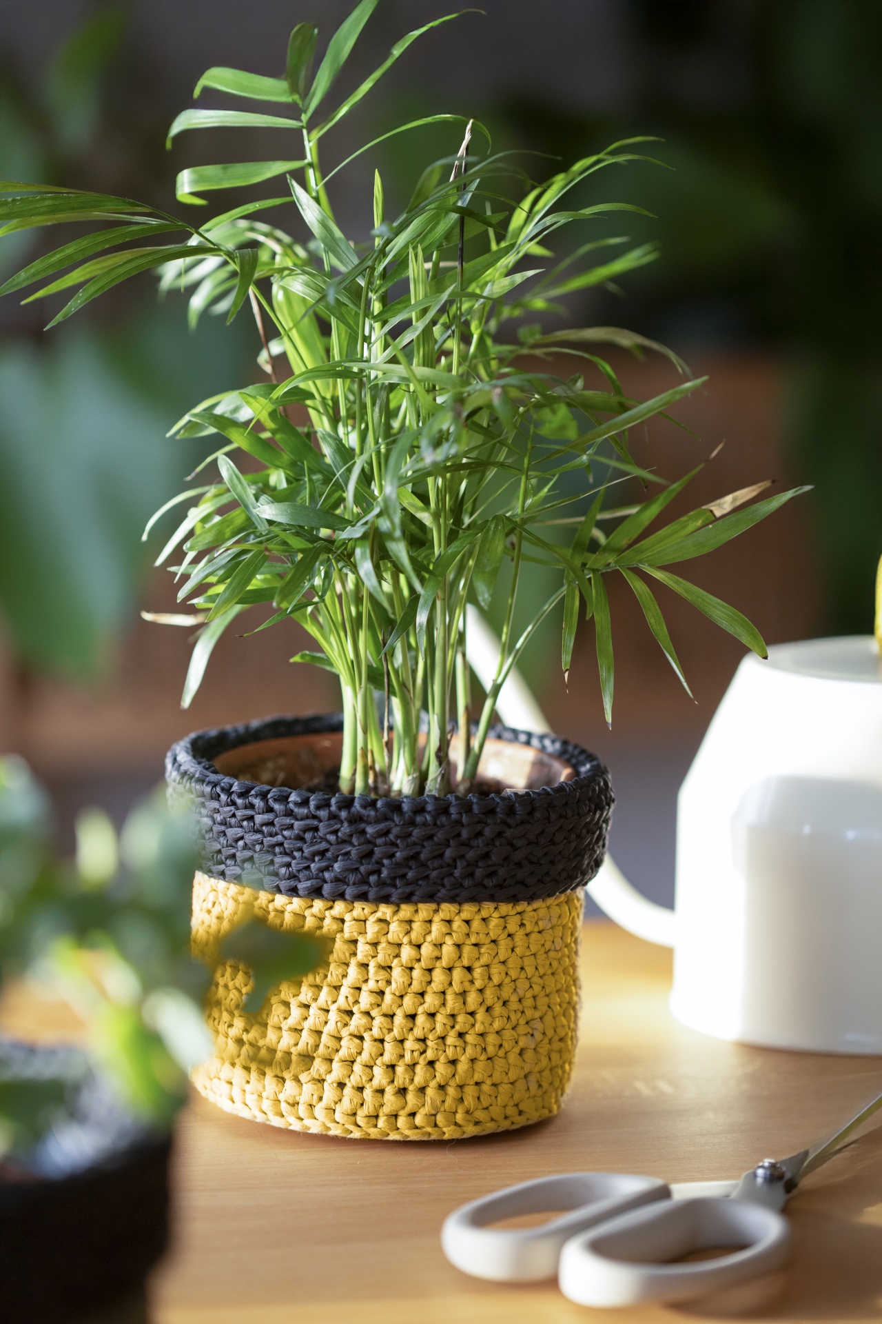 Planta em vaso tricotado amarelo e preto sobre mesa com tesoura branca e regador
