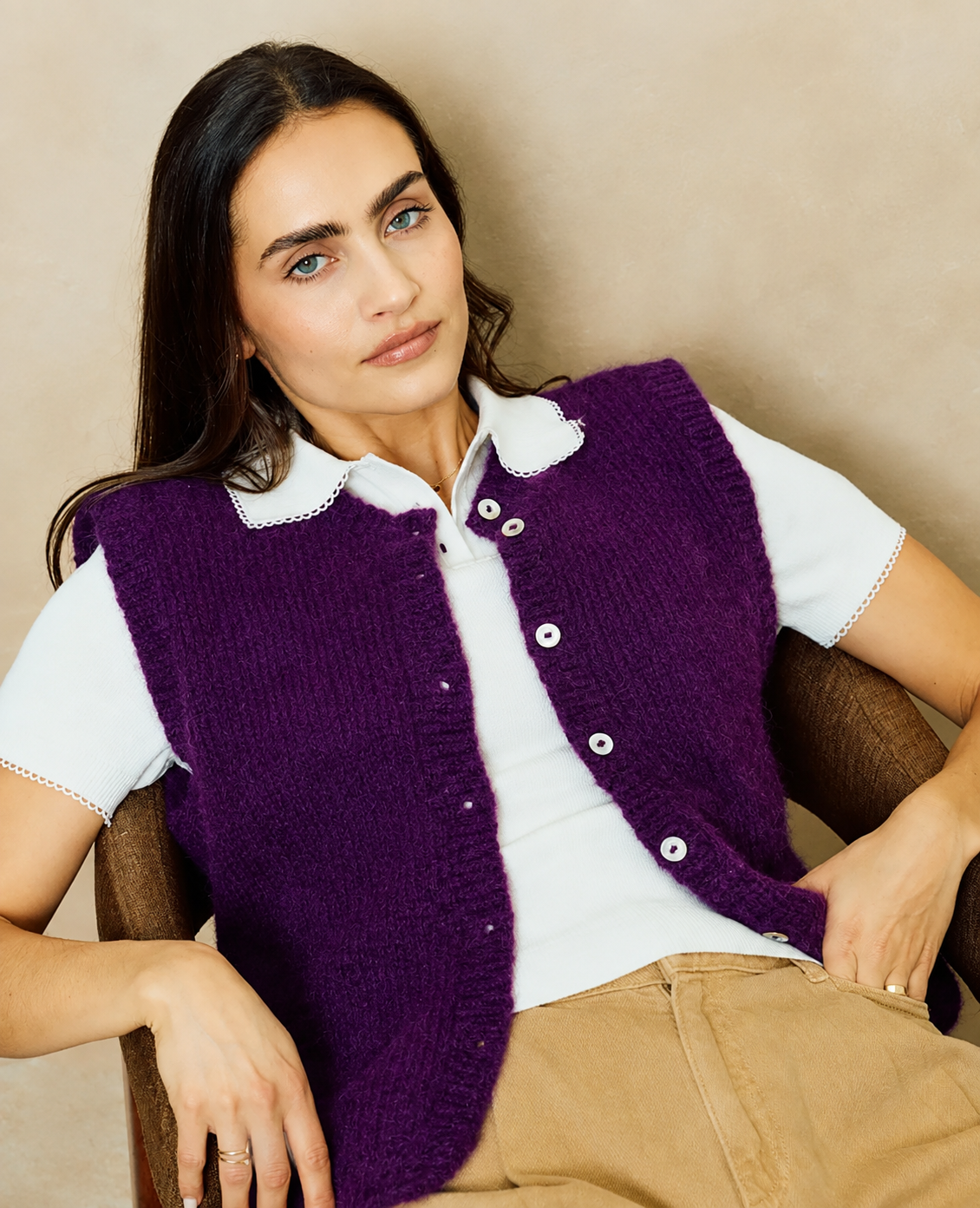 Mulher com colete roxo de malha e camisola branca sentada numa cadeira