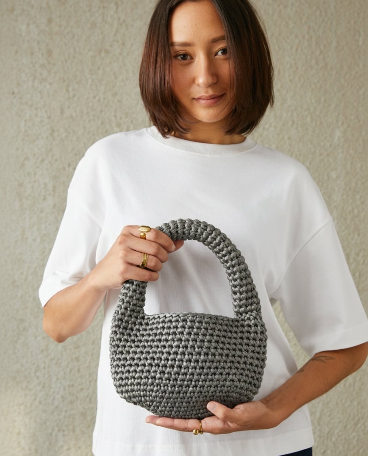 Mulher segura bolsa cinza tricotada com t-shirt branca