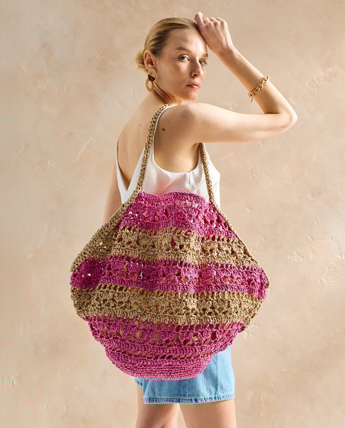 Mala de mão grande de croché rosa e bege em modelo com blusa branca e calções de ganga