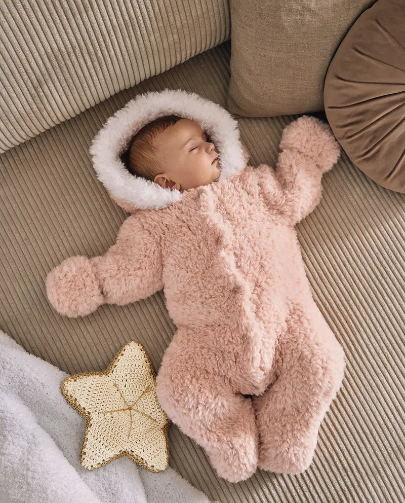Bebé a dormir com macacão felpudo cor-de-rosa com capuz e luvas integradas