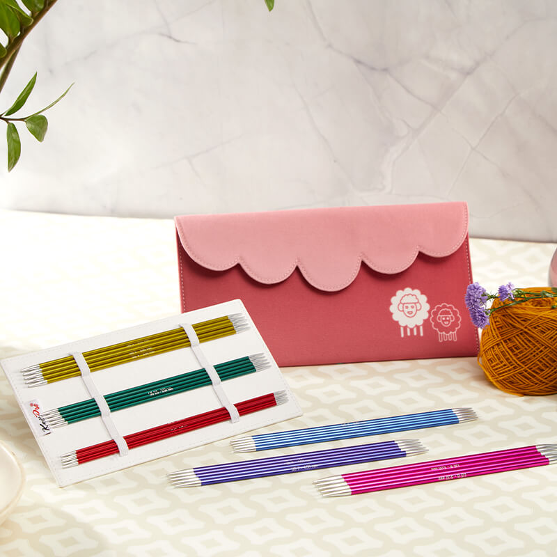 Carteira cor-de-rosa com agulhas de tricô coloridas espalhadas em superfície clara